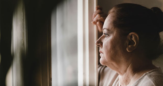 A mother that lost her child looking through a window with a sad facial expression