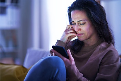 A sad mother using her phone while sitting on a couch after losing a child