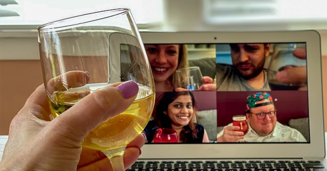 A woman holding a glass of white wine in front of her laptop during a virtual event meeting with oth...
