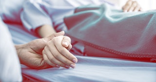 A man holding a woman's hand while she is lying in the hospital bed who's had an abortion