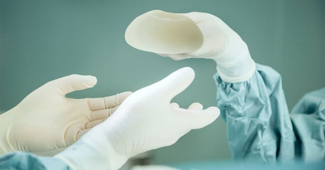 A person's hand in white gloves giving a breast implant to another doctor during a surgery