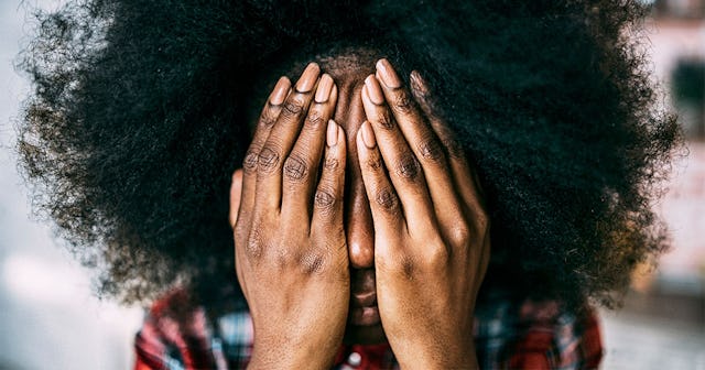 Curly-haired woman covering her face with her hands