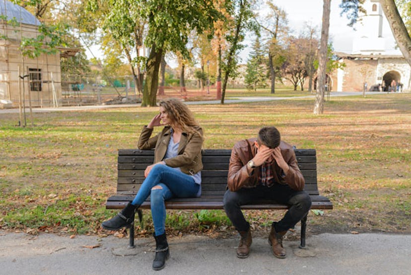 A woman sitting on a bench in a park next to her husband while both are in distress