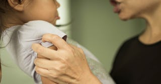 A mom wearing a black t-shirt screaming at her young daughter while holding her arms 