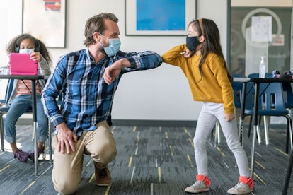 A teacher and a girl wearing masks and greeting each other with their elbows. 