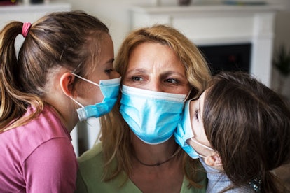 A single mom wearing a mask receiving kisses from her children, who are also wearing face masks
