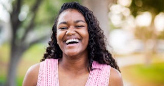 A girl smiling and looking to the camera wearing a pink top and afro curls