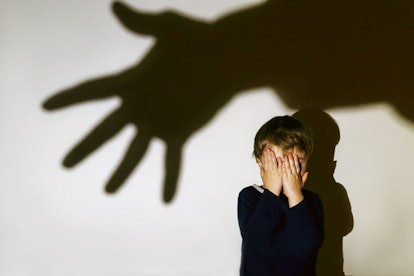Scared child hiding face behind his hands while the shadow of pedophile is reaching him