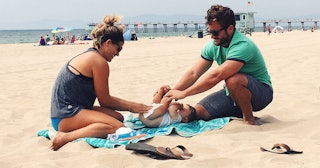 Young parents changing their baby's diapers on a beach