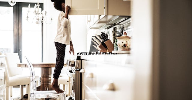 A girl in a white shirt and black sweatpants is standing on a chair reaching the upper part open cab...