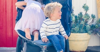 A blonde boy in a beige-navy sweater and blue denim jeans sitting in a stroller next to a girl in a ...