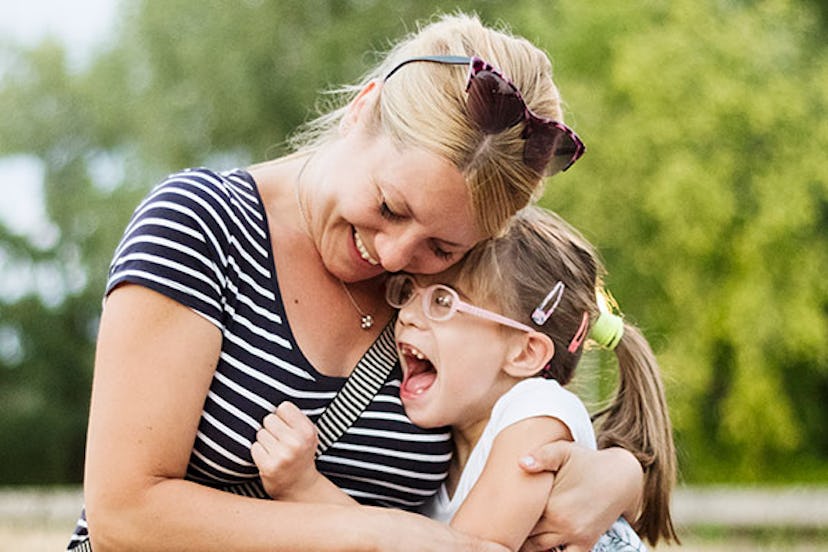 A blonde mother with sunglasses smiling while hugging her daughter with special needs on the bench i...