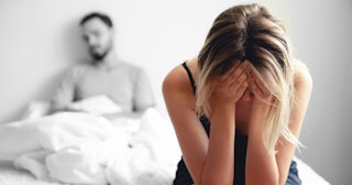 Woman crying on the bed and hating her husband after her miscarriages while her husband is sitting i...