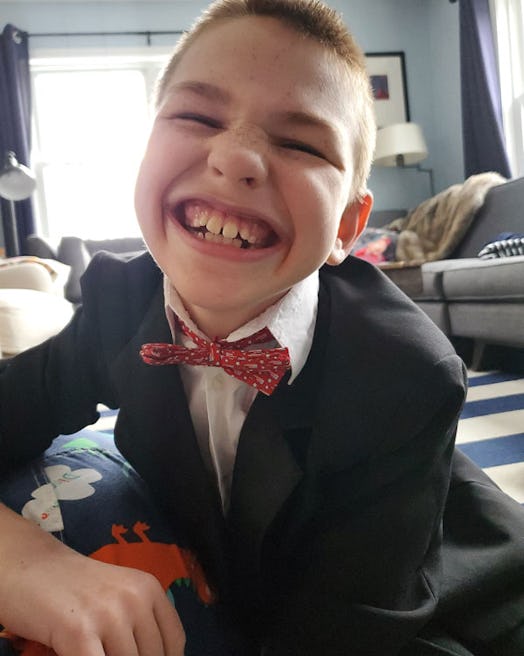 A boy with a vanishing white matter disease smiling while wearing a black suit in his living room