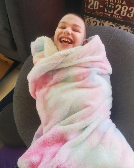 A boy with a vanishing white matter disease smiling wrapped up in a light pink blanket