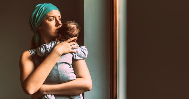 A woman in a grey shirt and a teal turban holding her baby while looking through a window with a wor...