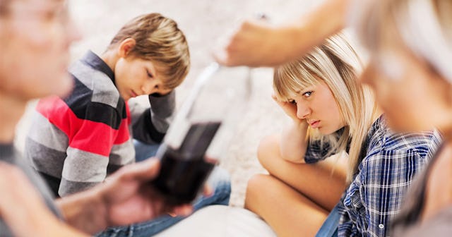 Two kids watching their parents hand each other a bottle of wine with appalled looks on their faces.