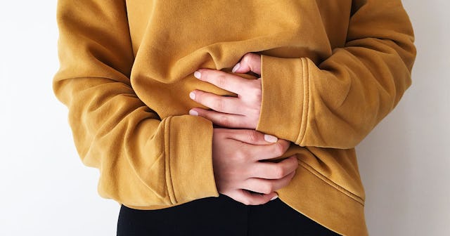 A woman in a mustard yellow hoodie with her hands on her stomach