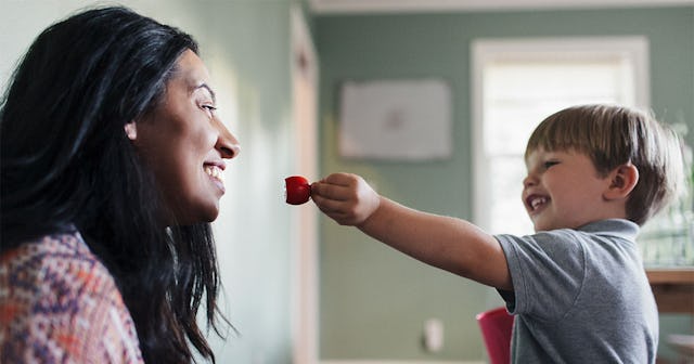 A boy in a grey T-shirt trying to give his stepmom a strawberry