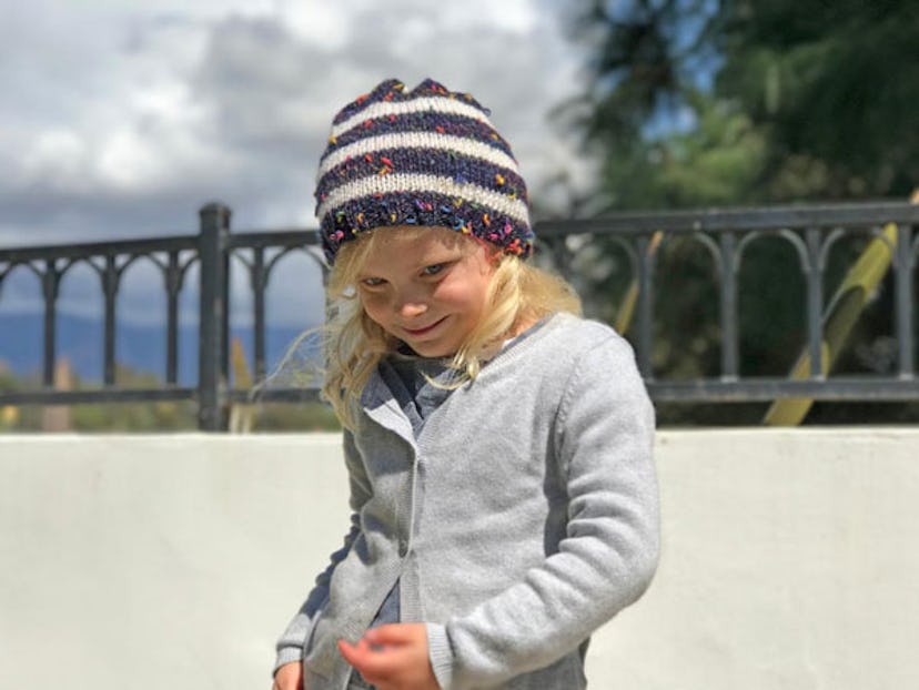 A little girl smiling in the gray sweater and colorful cap