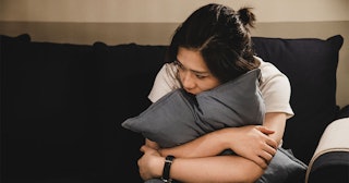 A sad daughter with an upset facial expression sitting hugging a pillow because of mother's death