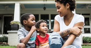 A mother sitting in front of the house and talking to her two little boys about toxic masculinity