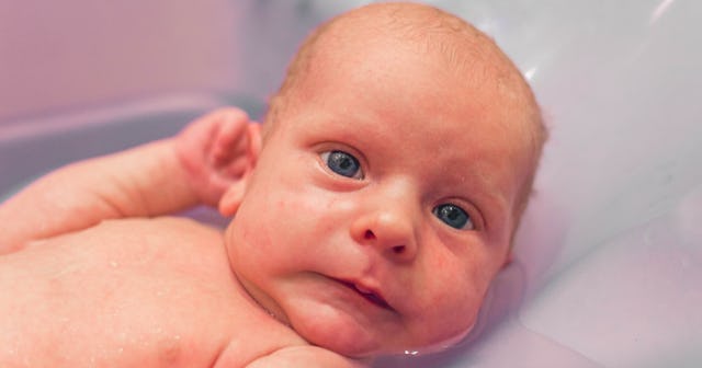 white baby looking concerned in the bath while holding ear