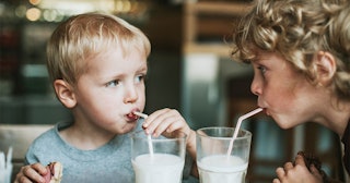 Two kids drinking breastmilk out of two glasses while looking at each other.