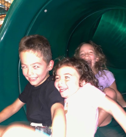 A boy in a black shirt and two girls in blue and lavender shirts laughing in a slide during a family...