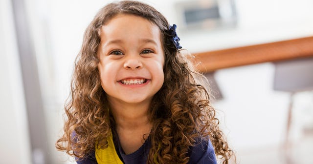 A biracial little girl with curly hair smiling 