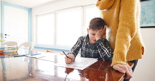 A mother in a yellow sweater helping her son with oppositional defiant disorder doing his homework.