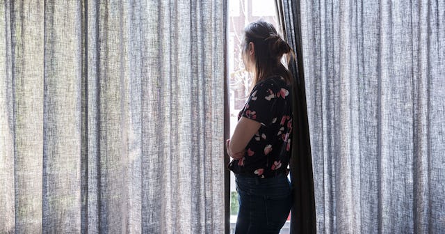 Woman standing in front of a window between the curtains