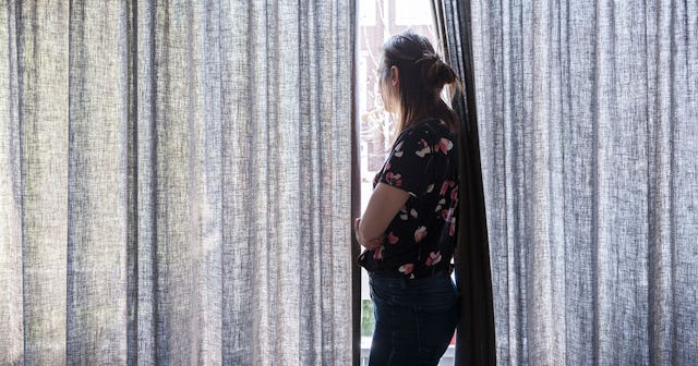 Woman standing in front of a window between the curtains 