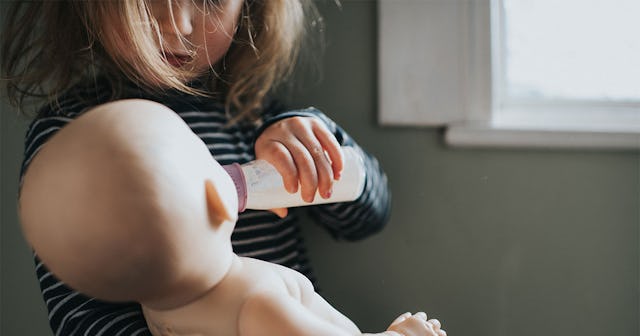 A little girl holding a bottle and feeding her baby doll