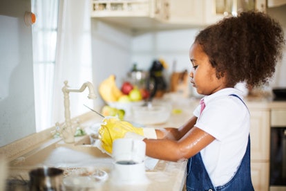 A little girl washing dishes in a kitchen 