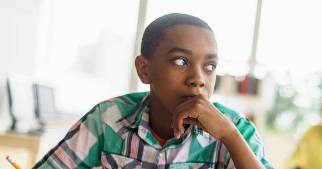 A tween boy in a green-pink-white checked short-sleeved shirt leaning his chin on his hands and look...