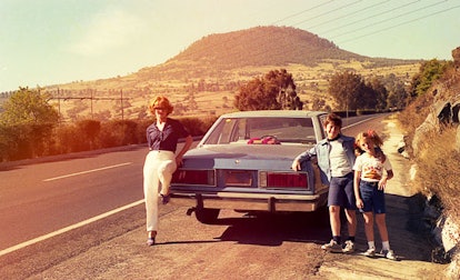 A mother, her son, and her daughter next to a car on the road 