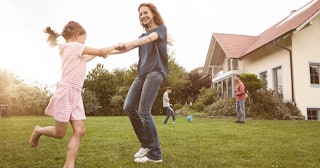 A stay-at-home mom playing with her daughter in the backyard, with her husband and son playing socce...