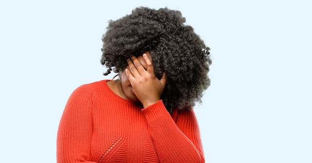 A curly-haired woman during her perimenopause covering her face with her hand