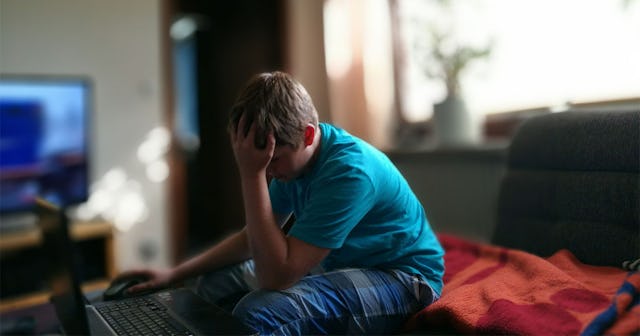 A boy sitting in front of the computer with his head down.