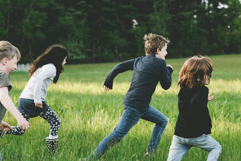 A group of children running on the grass with trees behind them