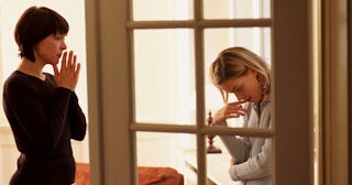 Two young women standing in an apartment feeling worried and stressed.