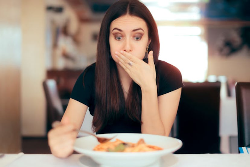 A woman holding her hand over her mouth in disgust over the food on a white plate in front of her on...