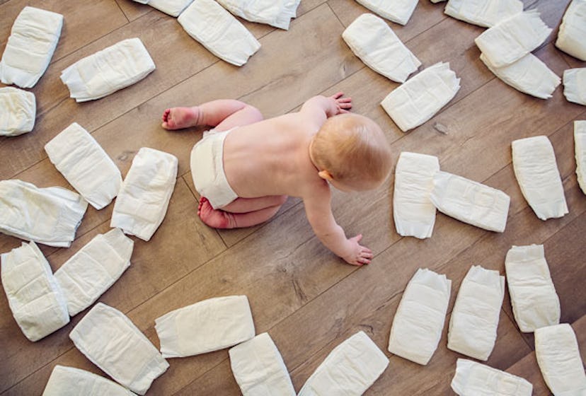 A child wearing a diaper, crawling on the  floor with diapers surrounding it 