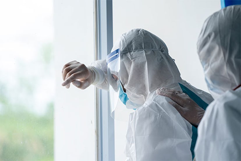  A doctor wearing a COVID protection suit looking out the window tiredly