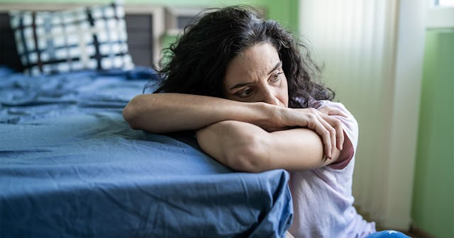 A woman sitting on the floor in the bedroom, leaning on the bed with her arms 