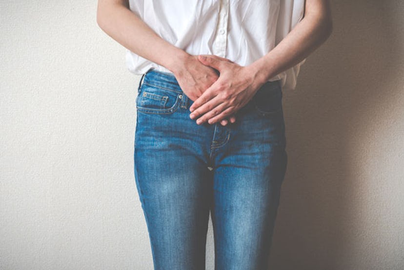 A woman dressed in jeans and white shirt, holding her stomach with her hands 