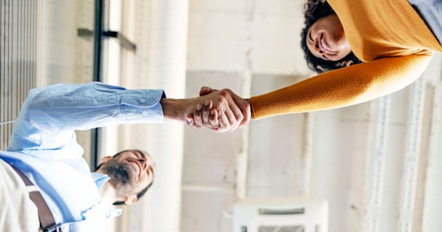 Man wearing a blue shirt and white pants and woman wearing an orange shirt shaking hands in a health...