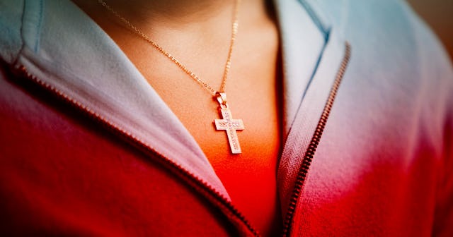 A close-up of a woman's neck wearing a necklace with silver cross