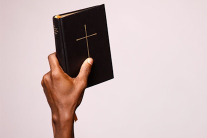 A hand holding the Bible with black covers and a golden cross in the middle.